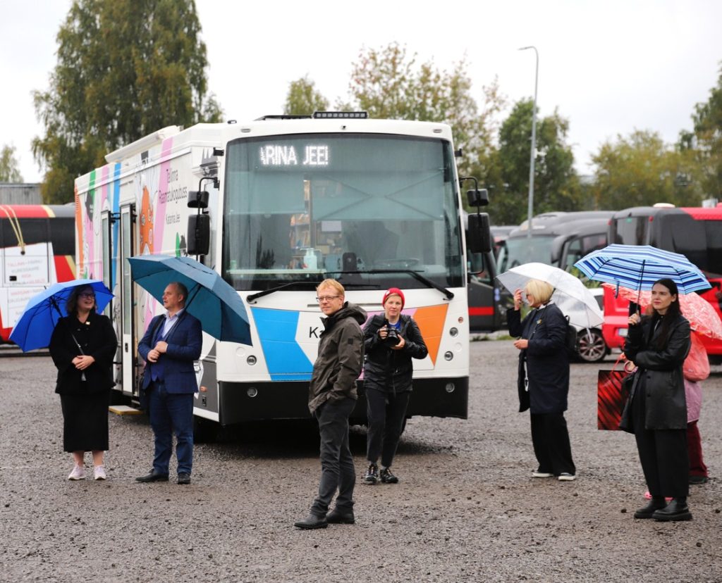 Inimesed seisavad uue raamatukogubussi ees porises prrklas. Kõigil on vihmavarjud, välja arvatud abilinnapea Kaarel Ojal ja fotograaf Ellen Rudil.