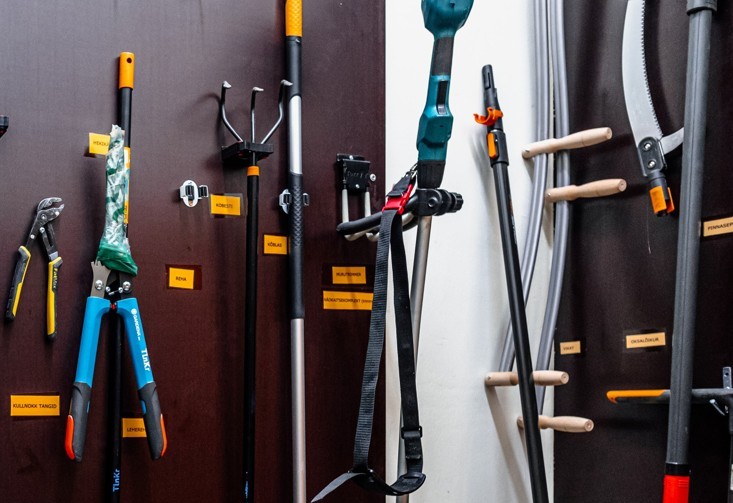 On the wall at the end of the screws hang various tools, e.g. pliers, secateurs, trowels, cordless trimmers, etc.